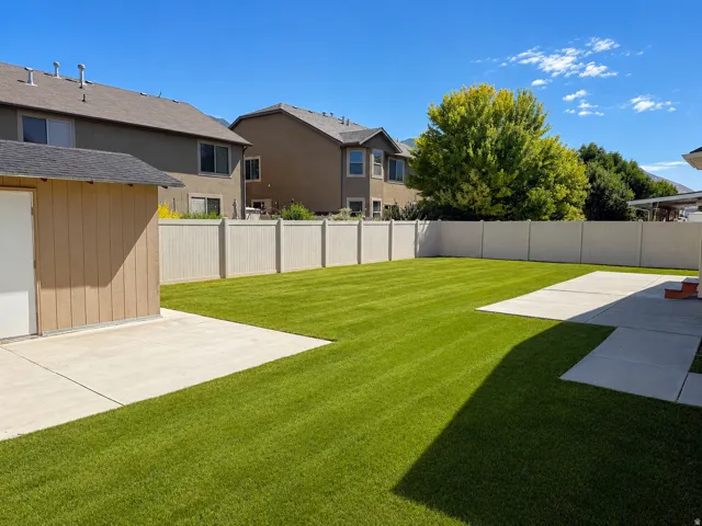 Expansive green lawn with a privacy fence, concrete patio areas, and a detached shed