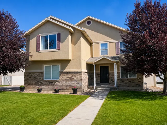 Two-story stucco and brick-finish exterior featuring a covered entry, established landscaping, and a concrete walkway