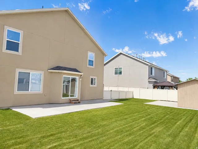 Expansive backyard featuring a manicured lawn, concrete patio, and mature privacy fencing