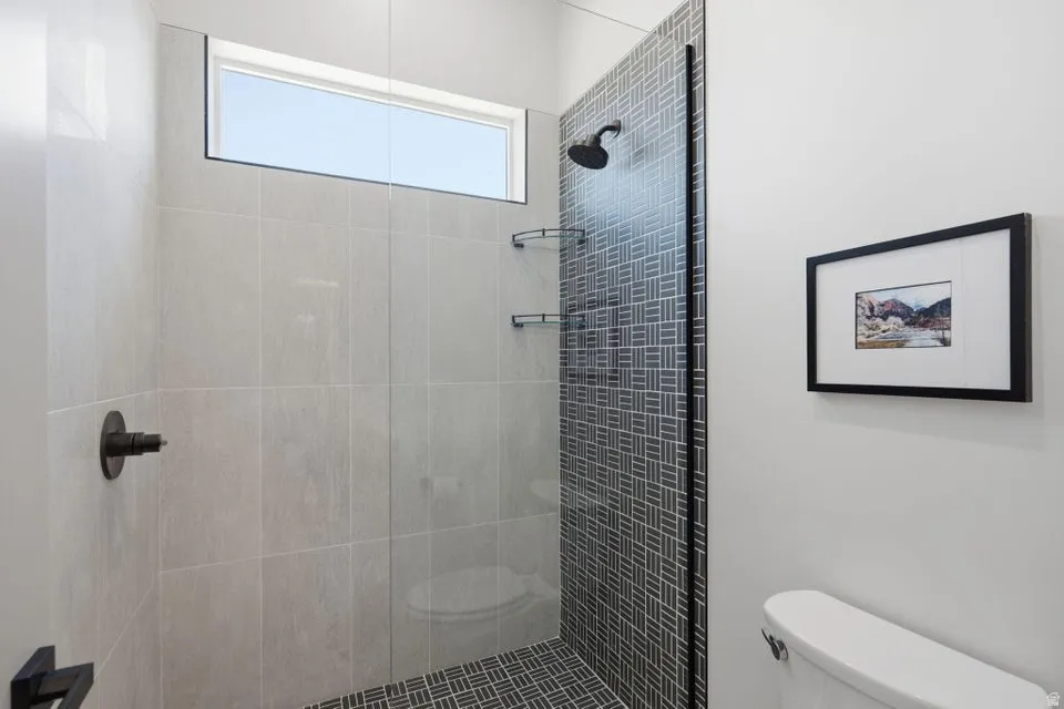 Walk-in shower featuring light-toned large format wall tiling, a dark-toned patterned accent wall, a fixed glass panel, matte black fixtures, and a transom window
