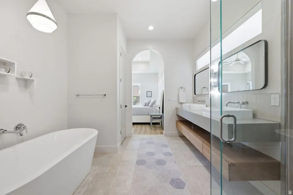 Bathroom featuring a freestanding soaking tub, dual vessel sinks, floating vanity with wood-finish drawers, and a walk-in shower with glass enclosure