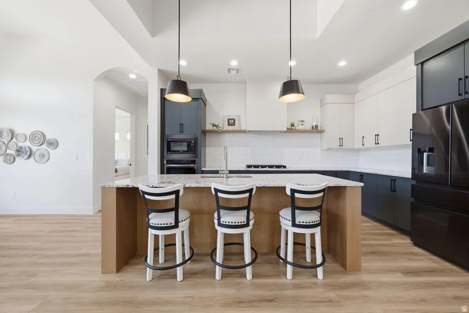 Kitchen featuring a large central island with seating, pendant lighting, built-in appliances, two-tone cabinetry, and wood-finish flooring