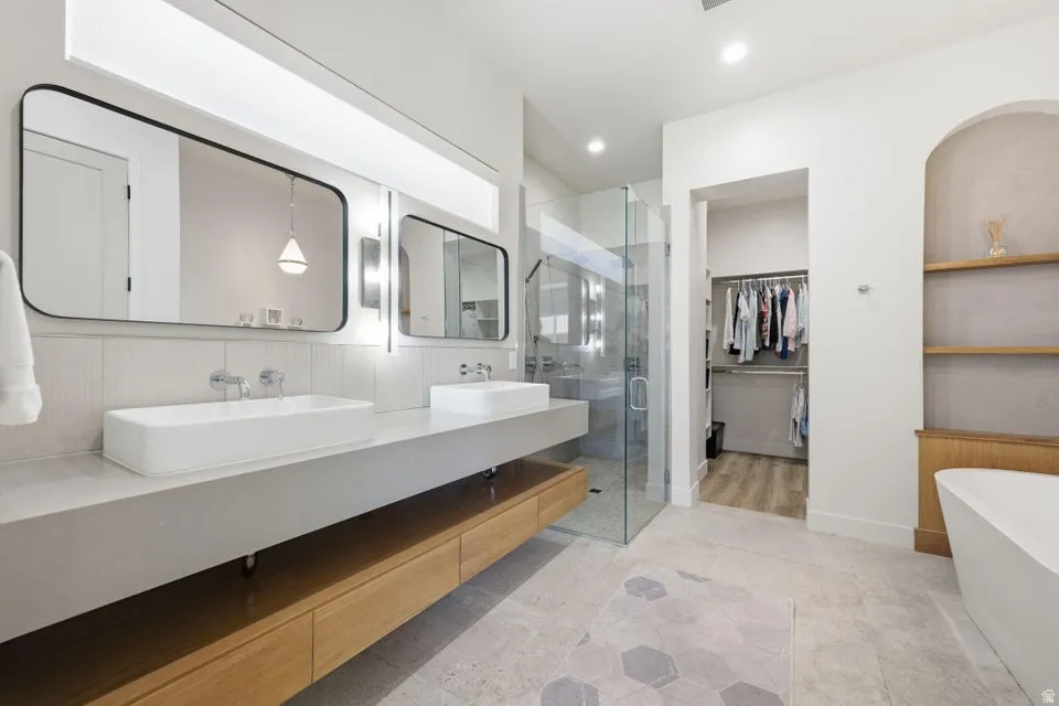 Modern bath featuring dual vessel sinks, floating vanity with wood-finish cabinetry, frameless glass shower enclosure, and a freestanding soaking tub