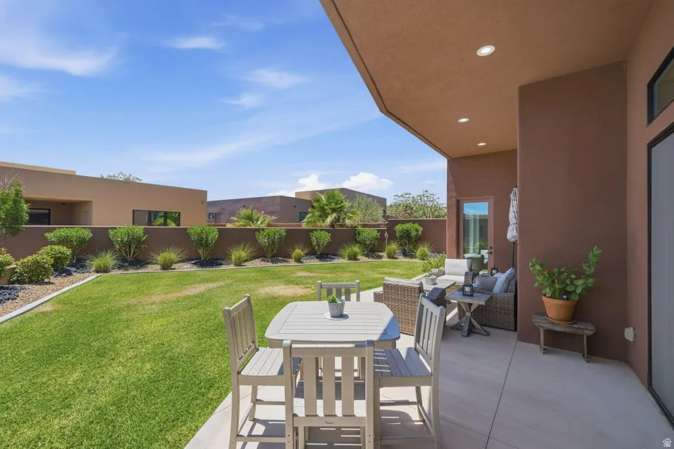 Private backyard featuring a covered patio, expansive lawn, mature shrubs, and an elevated perimeter wall