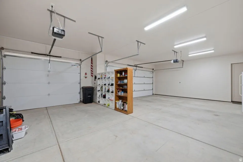Spacious two-car garage with concrete flooring, multiple overhead fluorescent light fixtures, and two overhead garage door openers