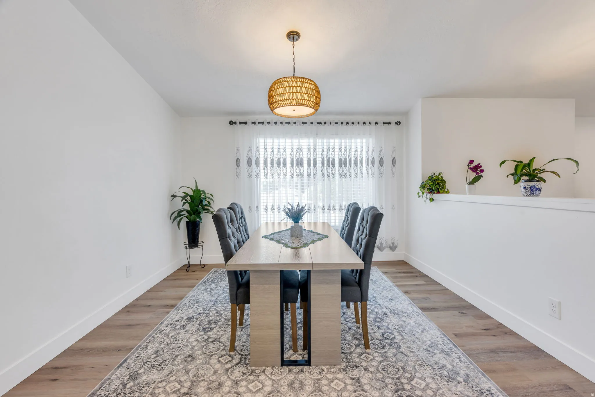 Dining area featuring wood-finish flooring, a contemporary woven pendant light fixture, and a large window with sheer curtains