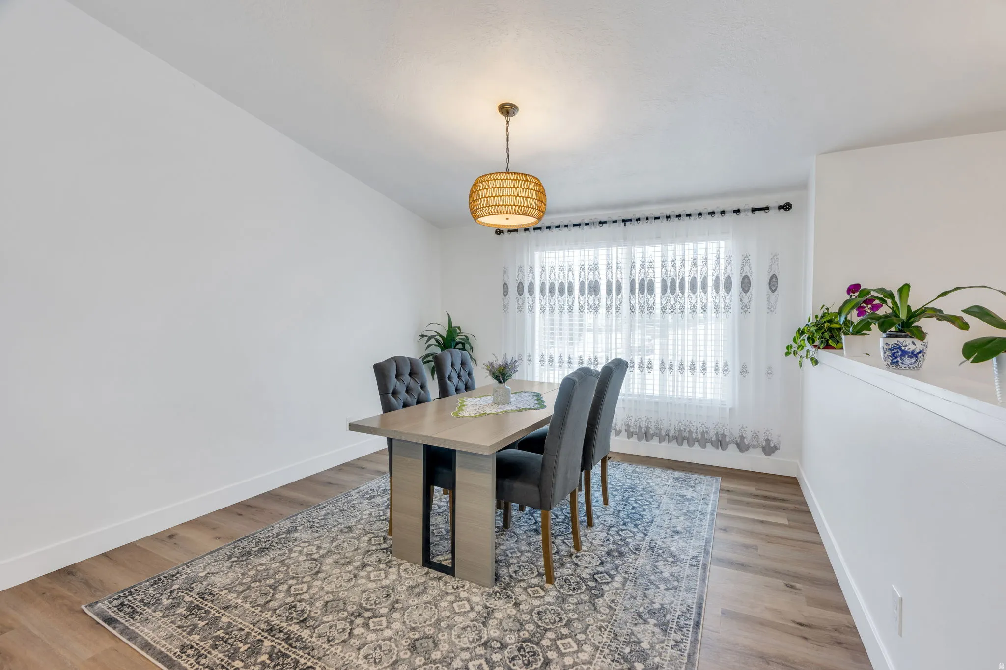 Bright dining area featuring wood-finish flooring, a contemporary pendant light fixture, and a large window with blinds