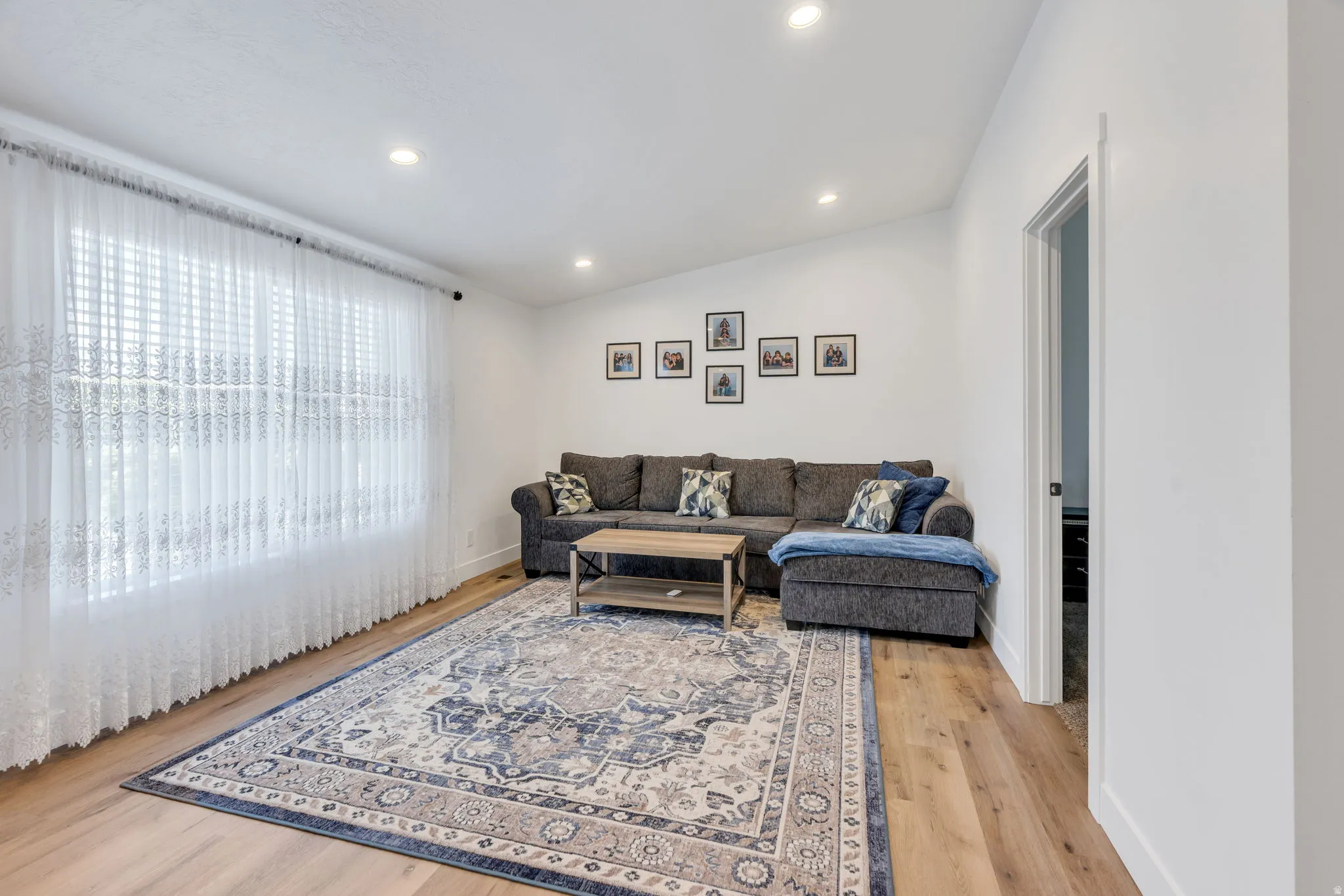 Bright living area featuring wood-finish flooring, recessed lighting, and a large window with blinds
