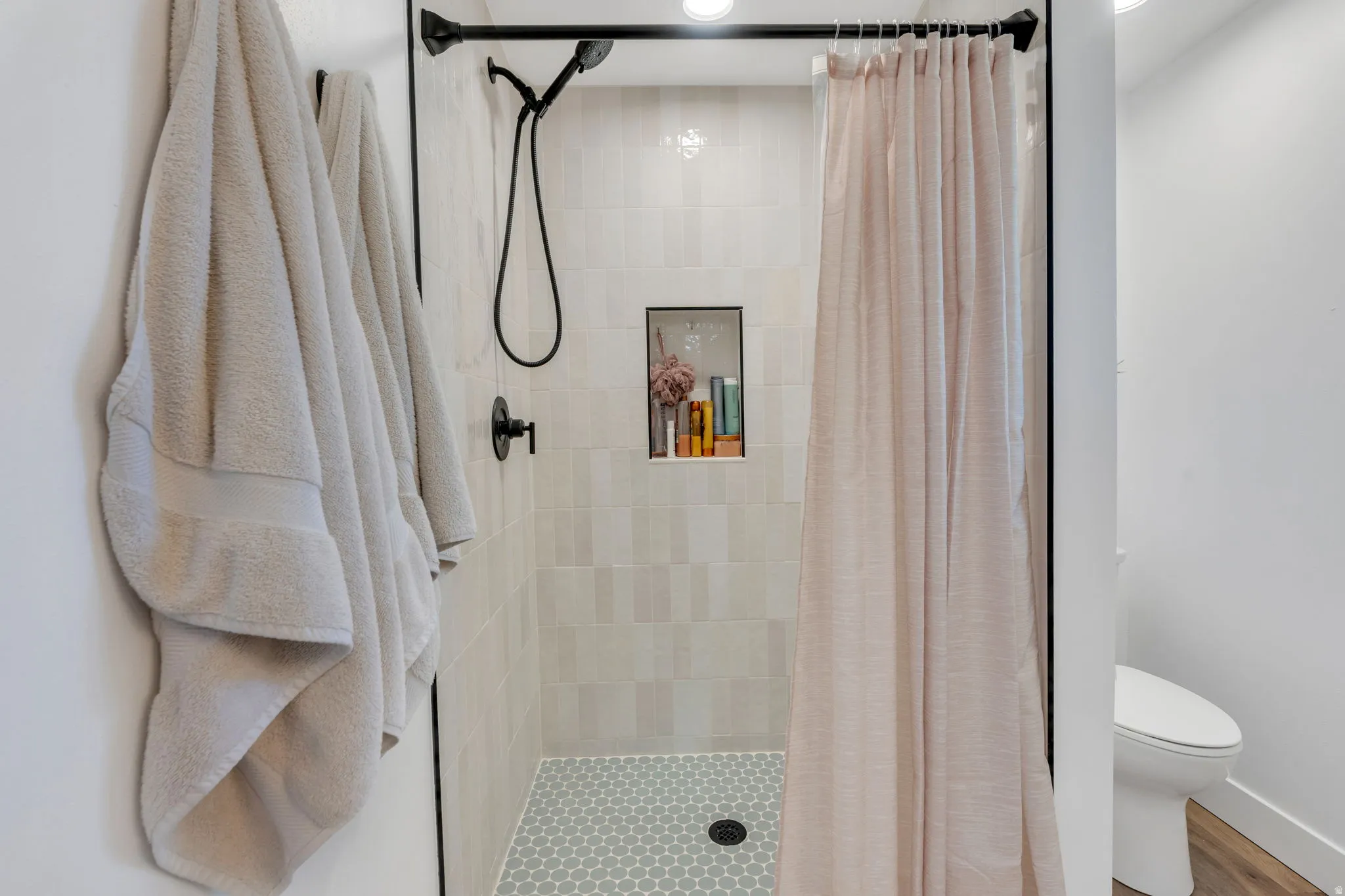 Tiled shower enclosure featuring light-toned rectangular wall tiles, a recessed niche, and a contrasting small hexagonal floor tile pattern