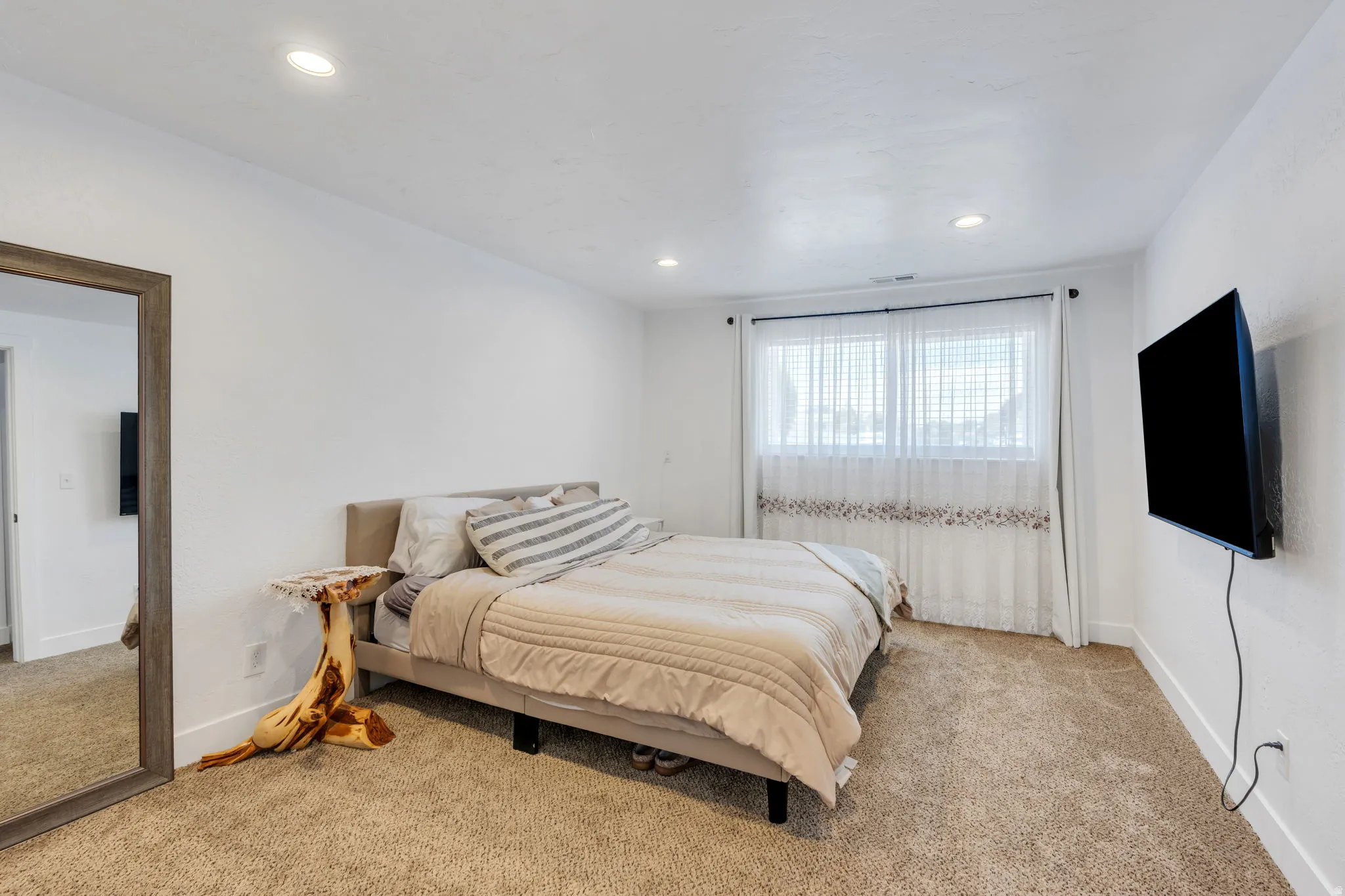 Carpeted bedroom featuring white walls, a window with horizontal blinds and sheer curtains, recessed lighting, and a wall-mounted television