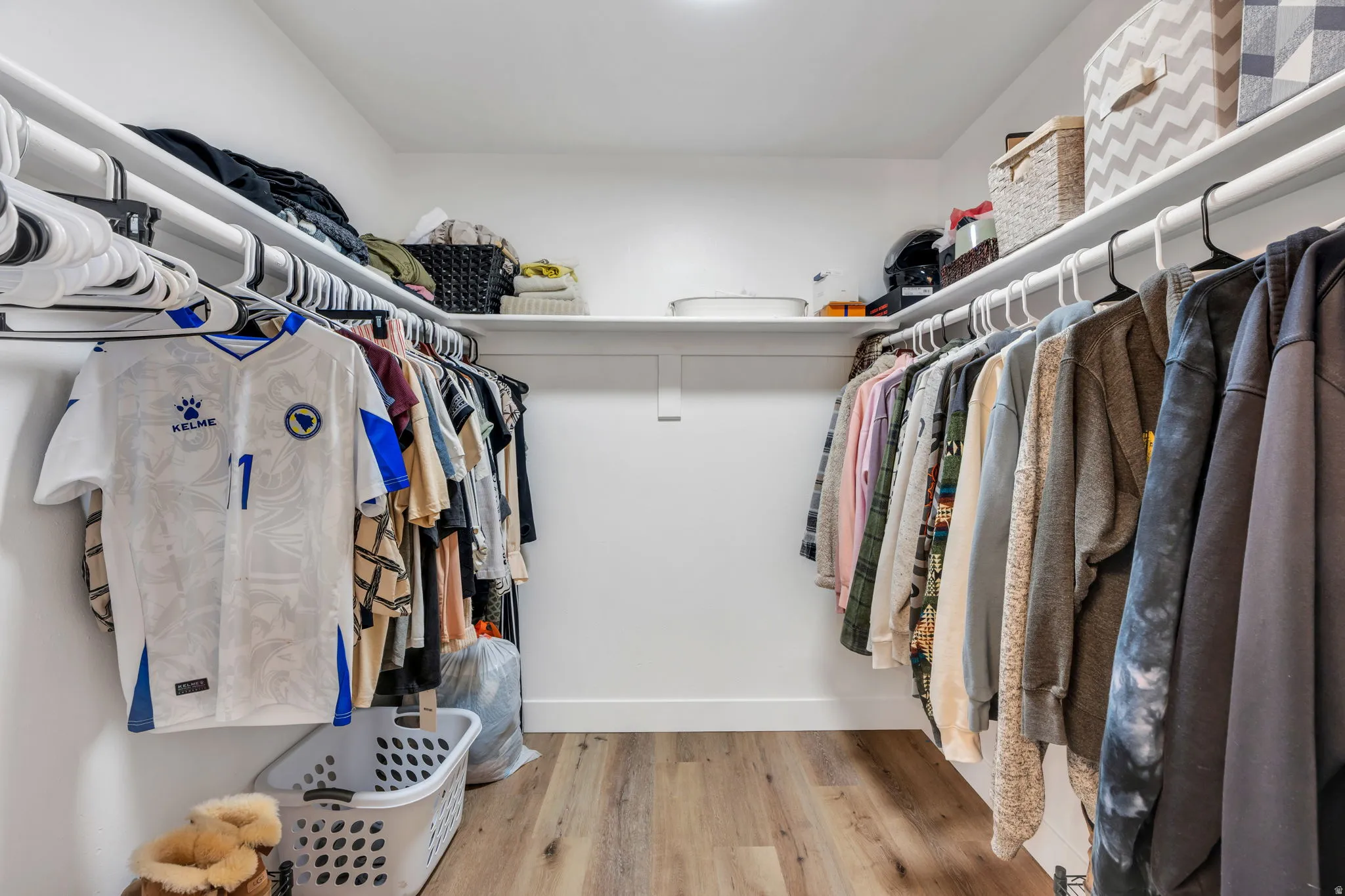Walk-in closet with ample shelving, multiple hanging rods, white walls, and wood-finish flooring