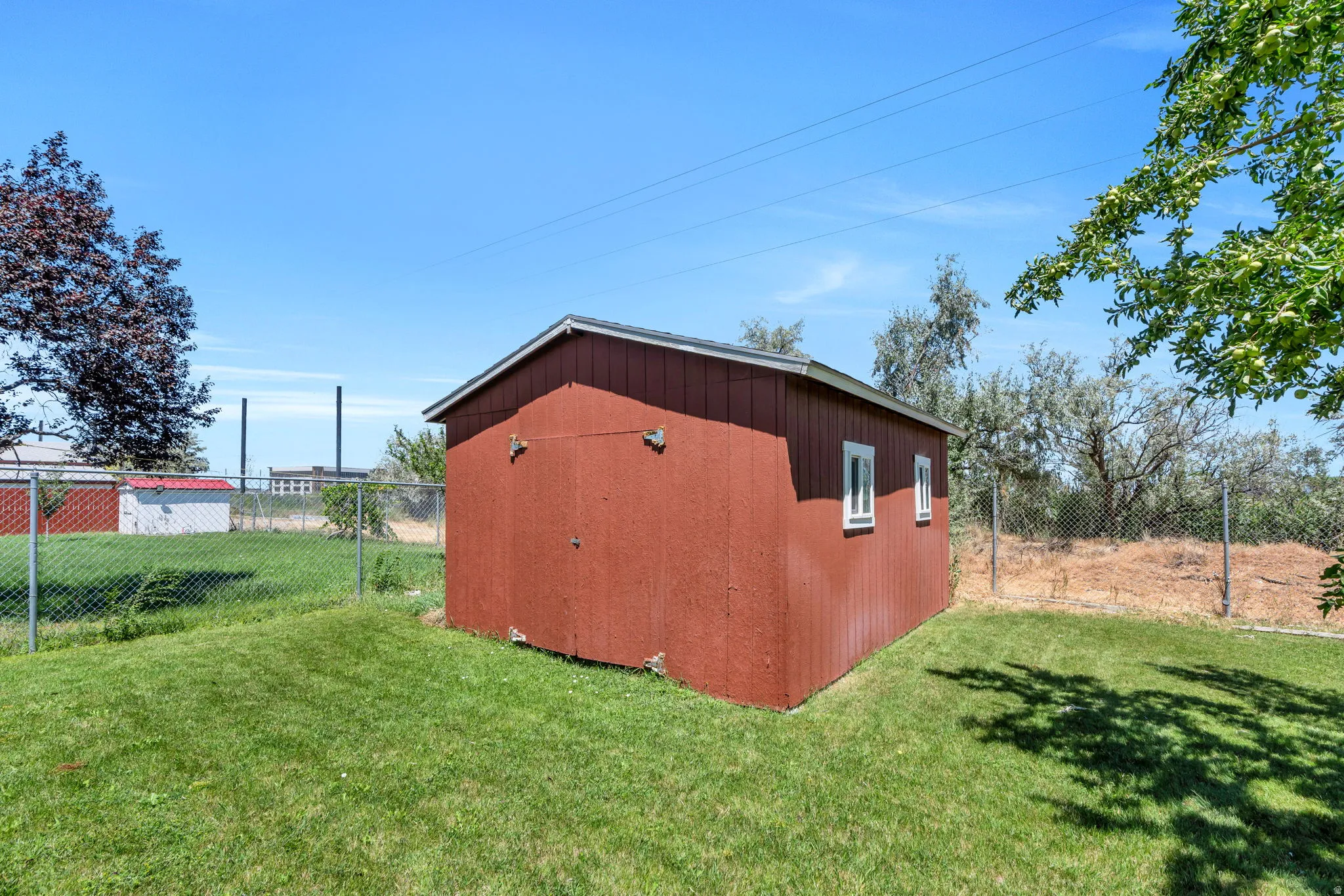 Exterior storage shed with a red finish, white trim windows, and a sloped roof