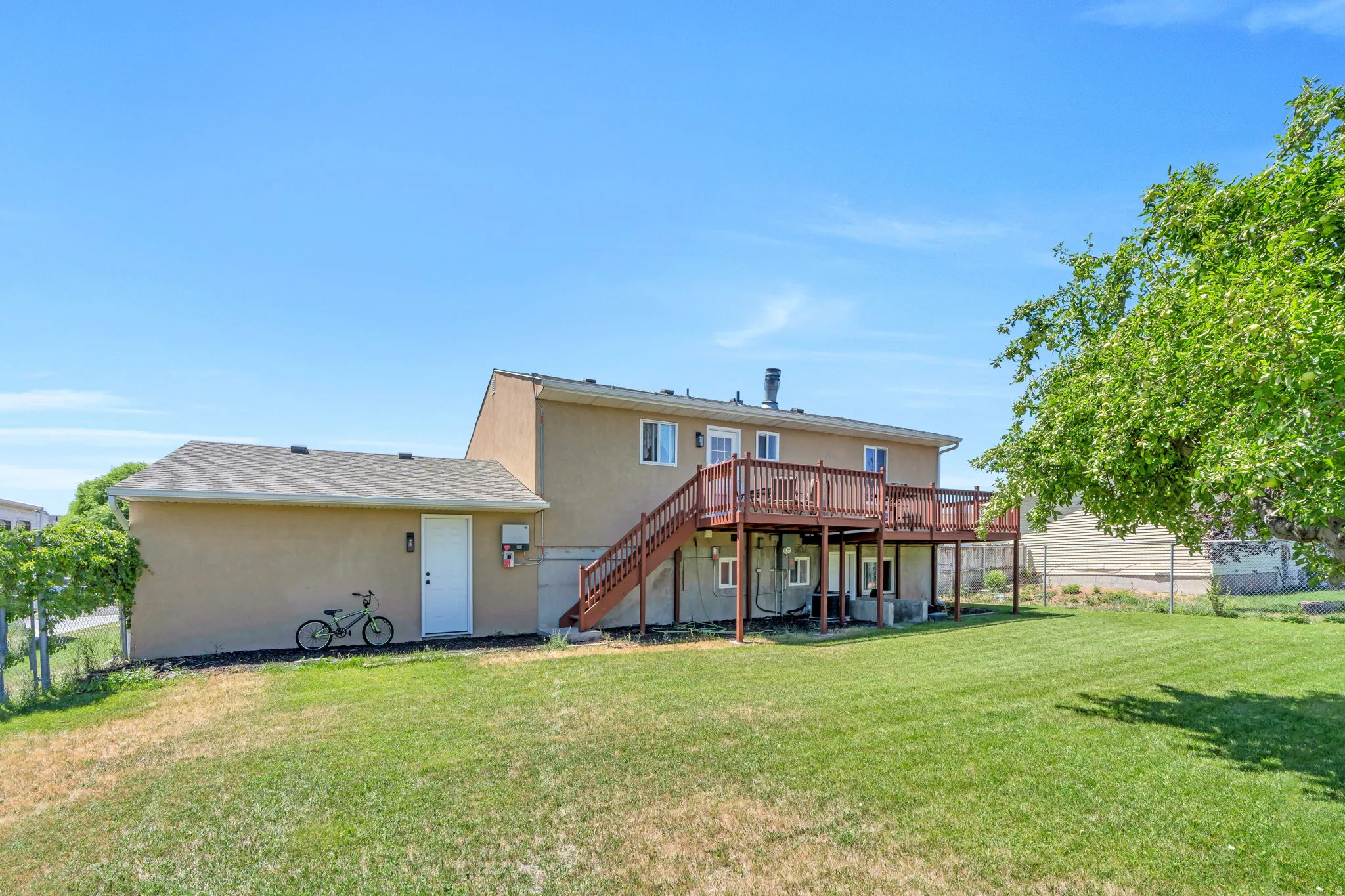 Expansive backyard with a two-story residence featuring a large wood deck with stairs, a lower-level concrete patio, and a separate single-story structure with an exterior door