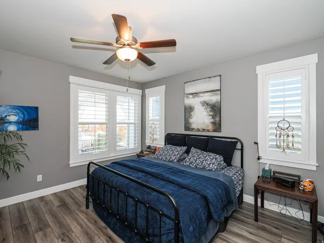 Wood-finish flooring, multiple windows with plantation shutters, ceiling fan with integrated lighting, and painted walls