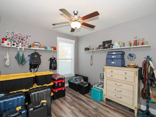 Wood-finish flooring, ceiling fan with integrated lighting, window with blinds, and wall-mounted shelving