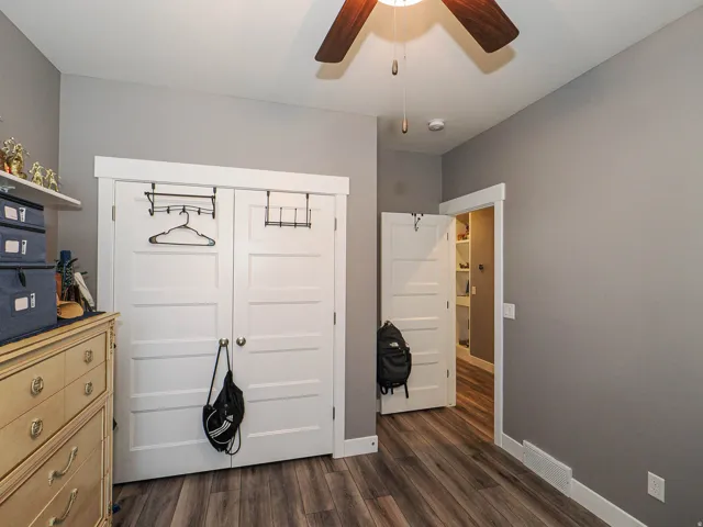 Wood-finish flooring, white panel doors, overhead ceiling fan, white baseboards, and built-in closet shelving