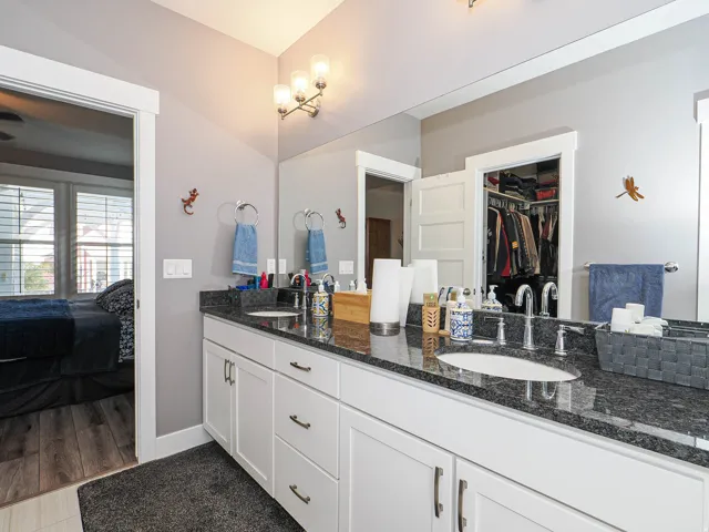 Dual vanity with a dark speckled countertop, white cabinetry, integrated sinks, and wall-mounted light fixture