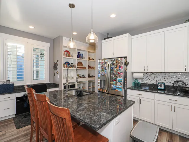 Kitchen featuring a large island with an undermount sink, white cabinetry, a mosaic tile backsplash, and built-in shelving