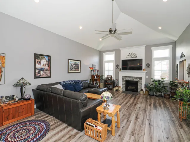 Vaulted ceiling with a ceiling fan, stone-clad fireplace with white mantel, wood-finish flooring, recessed lighting, and multiple windows