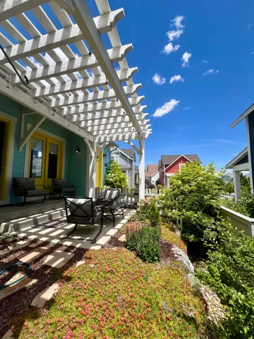 Expansive patio featuring a white pergola, concrete flooring, and vibrant landscaping