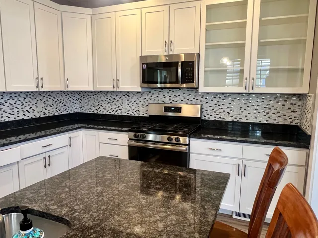 White shaker-style cabinetry, black countertop, mosaic tile backsplash, stainless steel appliances, and a kitchen island with an undermount sink