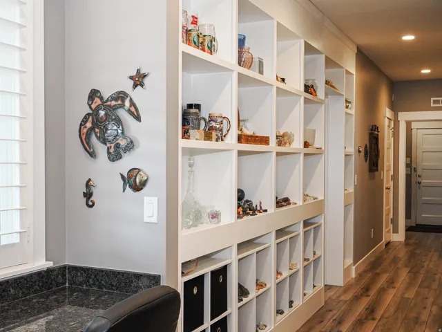 Built-in shelving with varied cubby sizes, natural wood-finish flooring, recessed lighting, white interior doors, and a dark stone-finish countertop