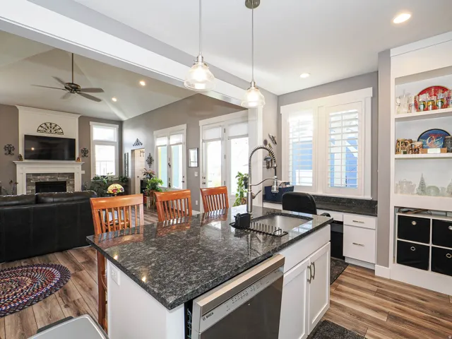 Kitchen island with dark countertop and integrated sink, stainless steel dishwasher, wood-finish flooring, white built-in shelving, and recessed lighting