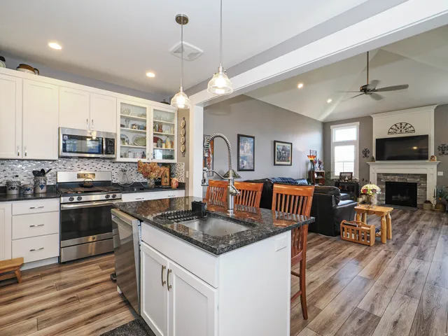 Open-concept living space featuring wood-finish flooring, a kitchen island with granite countertop, stainless steel appliances, and a gas fireplace with a stone surround