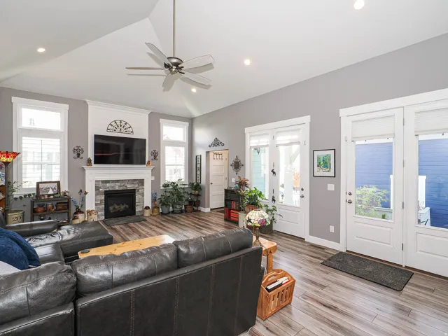 Vaulted ceiling with recessed lighting and ceiling fan, stone-surround fireplace with mantel, wood-finish flooring, and multiple glass-paneled exterior doors