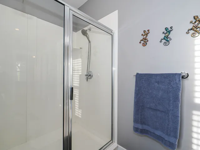 Enclosed shower with a clear glass and chrome frame, a handheld showerhead, and a built-in shower shelf