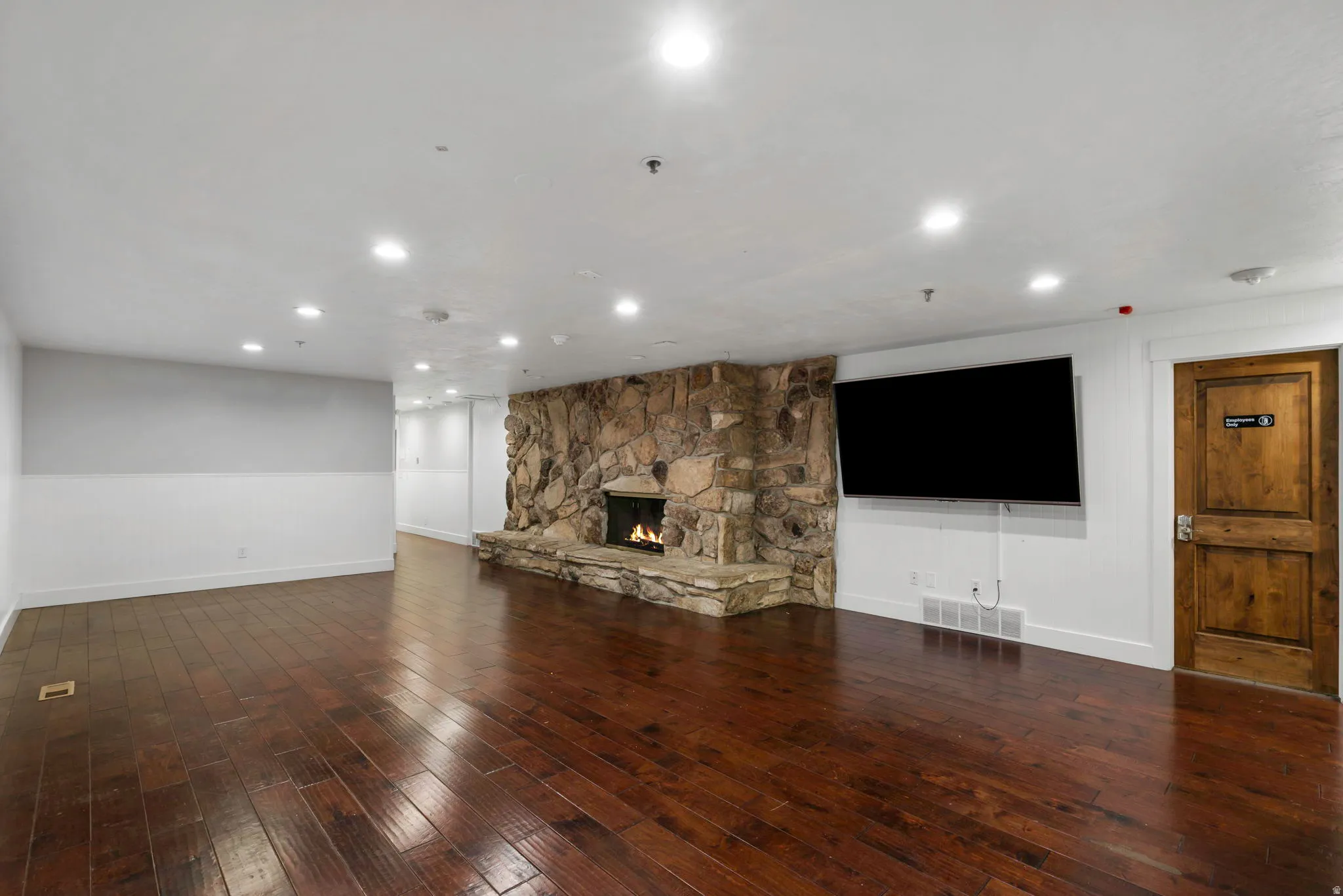 Expansive living area featuring rich wood-finish flooring, a stone-clad fireplace, and recessed lighting