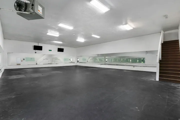 Spacious interior room with dark flooring, extensive wall-mounted mirrors, and an exposed wood staircase