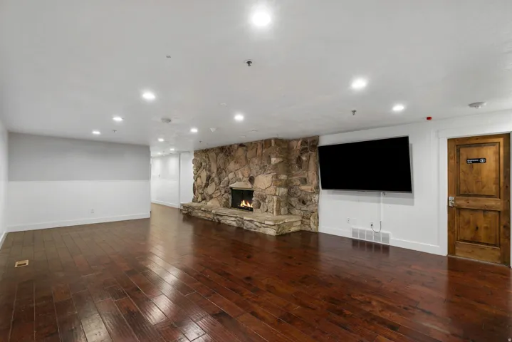 Expansive living area featuring rich wood-finish flooring, a stone-clad fireplace, and recessed lighting