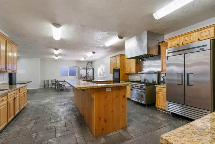 Spacious commercial-grade kitchen featuring extensive wood cabinetry, granite-finish countertops, stainless steel appliances, and durable tile flooring