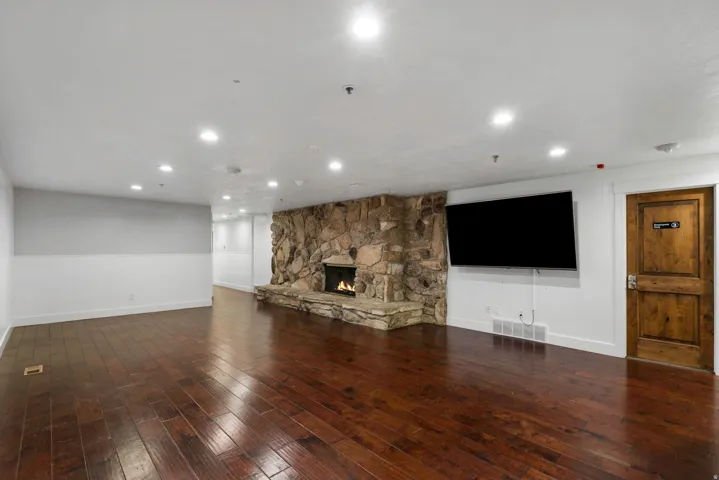 Spacious room featuring rich wood-finish flooring, a prominent natural stone fireplace, and recessed ceiling lighting