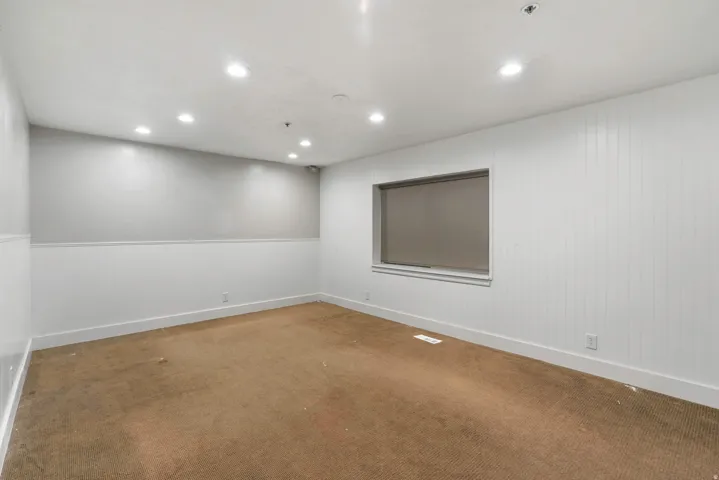Recessed lighting illuminates this room featuring light gray and white two-tone walls, white baseboards, and a window with a roller shade