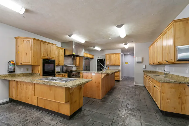 Professional kitchen featuring light wood cabinetry, granite-style countertops, integrated stainless steel appliances, and dark gray stamped concrete flooring