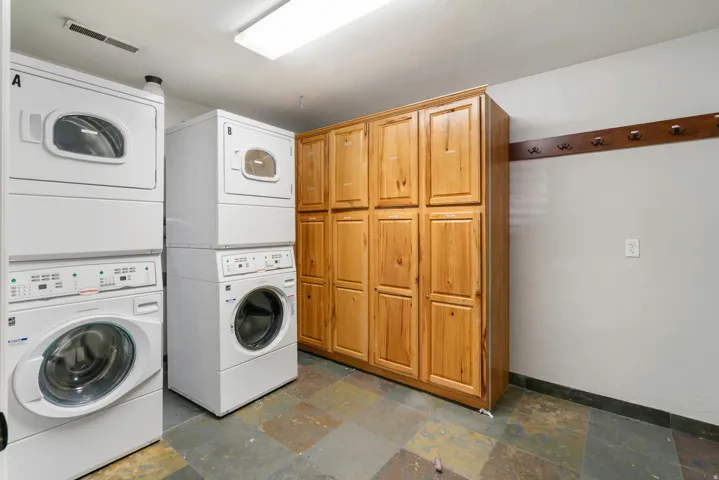 Dedicated laundry area featuring two stacked washer/dryer units, extensive wood cabinetry, varied natural stone flooring, and a wall-mounted wooden coat rack