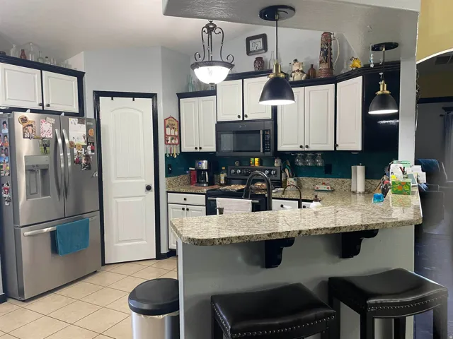 Well-appointed kitchen featuring a granite-style countertop peninsula with seating, contrasting dark and white cabinetry, recessed lighting, and tile flooring