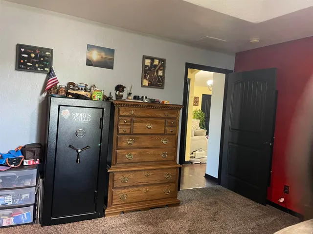 Carpeted room with a black paneled door and doorway revealing wood-finish flooring in an adjacent area