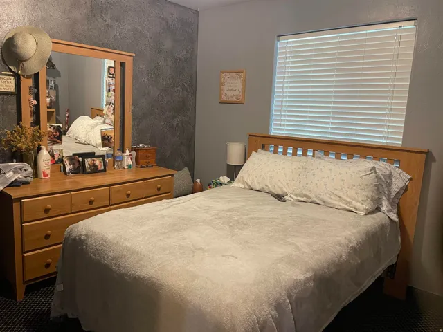 Bedroom featuring a textured accent wall, light-toned window blinds, a wood-finish headboard, and dark flooring