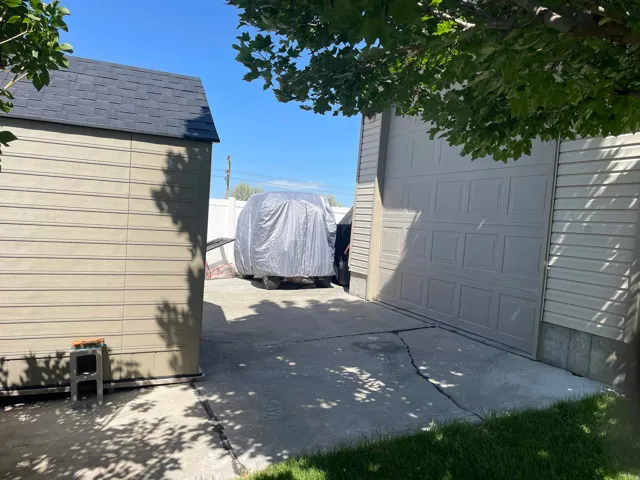 Concrete driveway with a detached storage shed featuring a shingled roof and horizontal siding