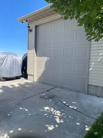 Garage structure featuring horizontal siding, a paneled garage door, and an exterior wall lantern
