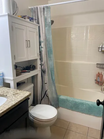 Bathroom featuring a built-in tub and shower combination with white tiled surround, tiled flooring, a white toilet, and a vanity with a granite-style countertop