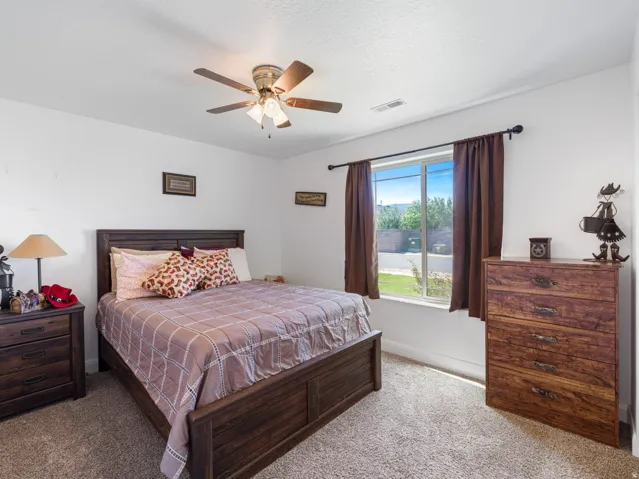 Bedroom featuring a ceiling fan with integrated lighting, a large window with brown drapes, and neutral carpet flooring