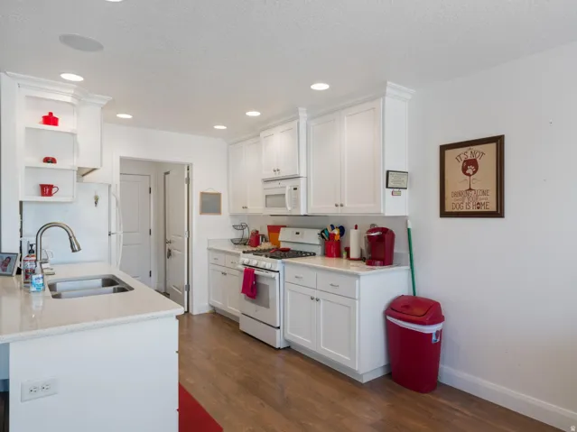Kitchen featuring white cabinetry, light-toned countertops, a stainless steel sink with a gooseneck faucet, a white gas range, and wood-finish flooring