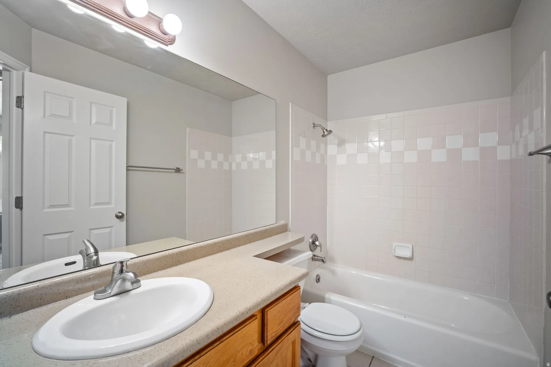 Full-width vanity mirror, integrated sink, wood-finish cabinetry, tiled shower surround with accent band, and chrome fixtures