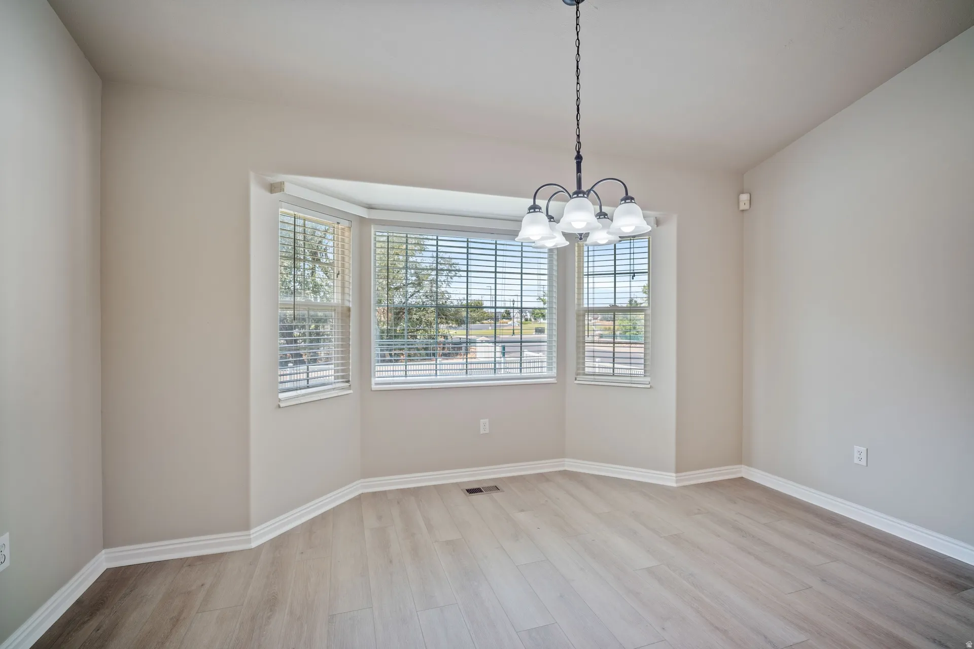 Bay window with blinds, wood-finish flooring, and a five-light chandelier
