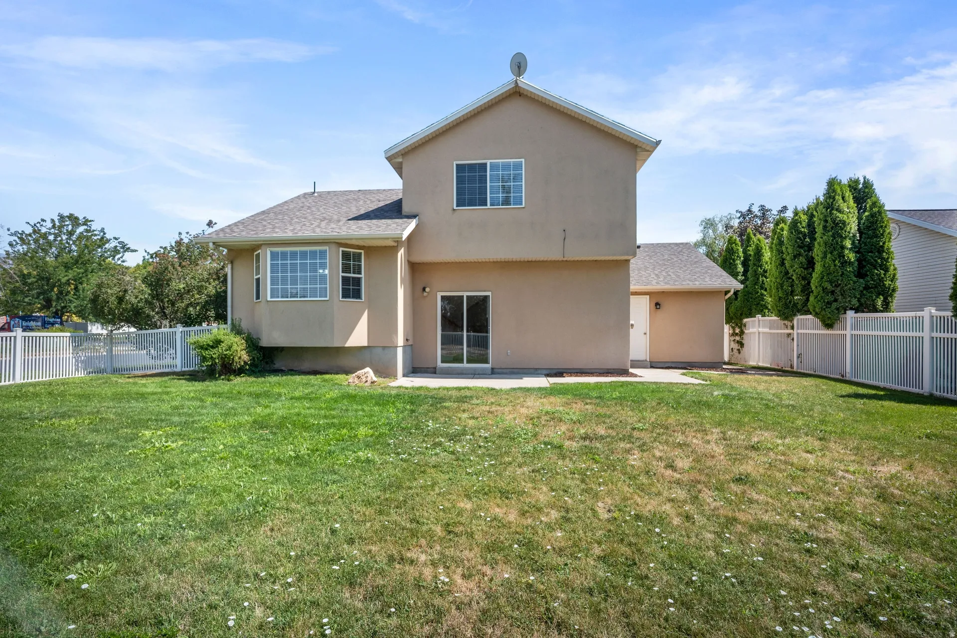 Expansive lawn area with a white privacy fence, bay window, and sliding glass door leading to a patio