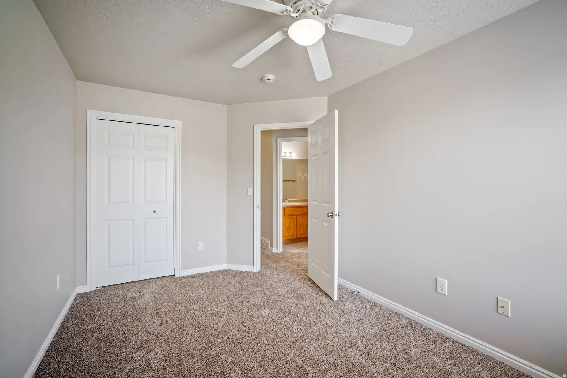 Neutral wall colors, carpeted flooring, a ceiling fan with integrated lighting, and a bi-fold closet